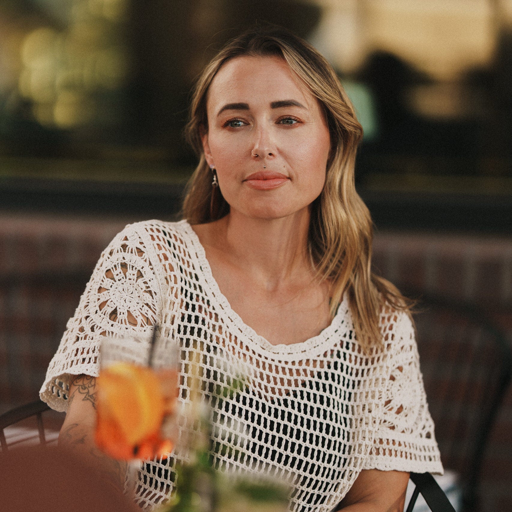 Woman sitting outdoors with drinks, wearing a white crochet top.