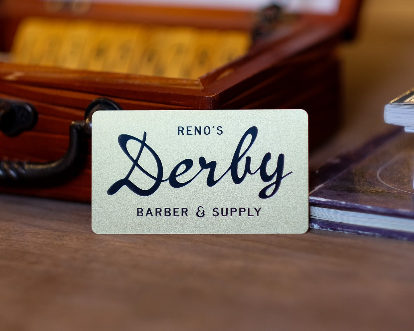 A gold membership card labeled 'DERBY BARBER & SUPPLY' placed on a wooden surface, indicating premium access or loyalty status.