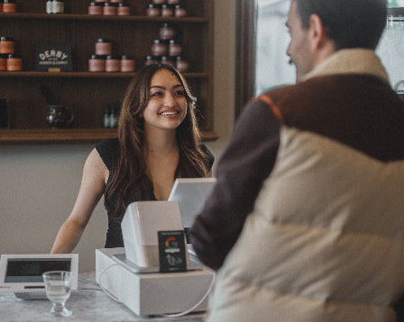 Woman behind a counter interacting with a customer in a cozy indoor setting.